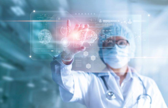 Un médico con mascarilla y gorro interactúa con una interfaz médica holográfica del Boletín Médico EuroEspes Health, que muestra imágenes y datos cerebrales. El entorno futurista sugiere tecnología avanzada en un laboratorio médico de vanguardia.