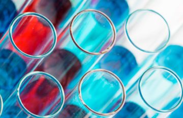 Primer plano de varios tubos de ensayo que contienen líquidos de color azul y rojo vibrantes, que recuerdan a un diseño del Boletín Médico. Los tubos de ensayo están dispuestos en filas, creando un patrón superpuesto que refleja el enfoque sistemático de EuroEspes Health.